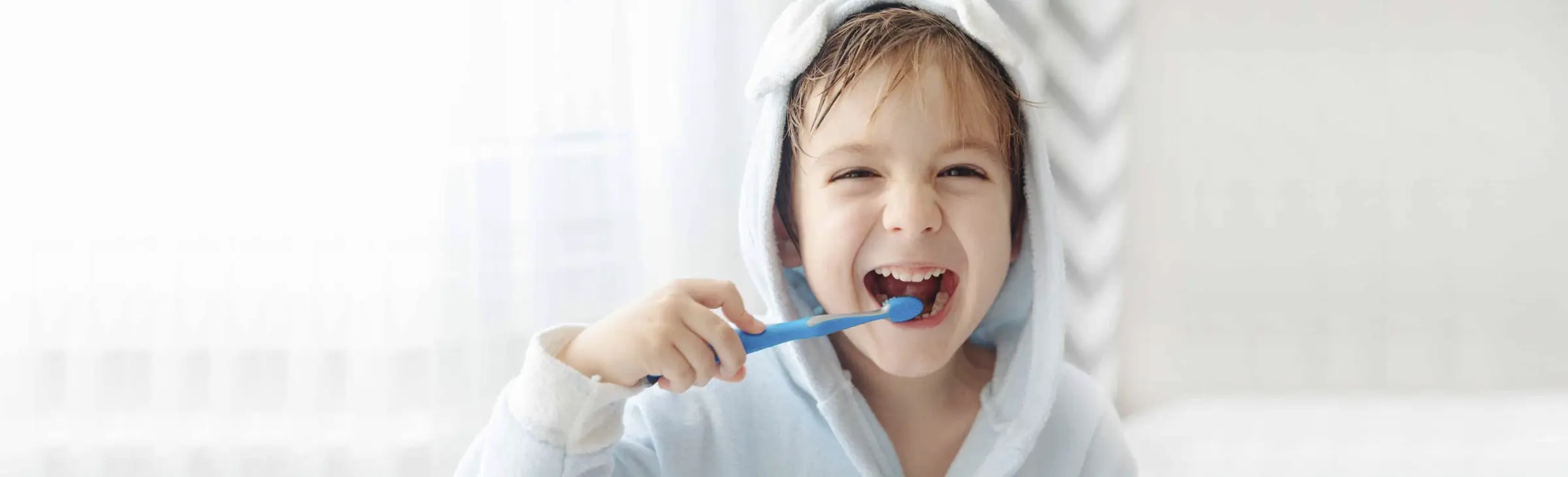 Happy child brushing teeth with blue toothbrush after fluoride treatment.