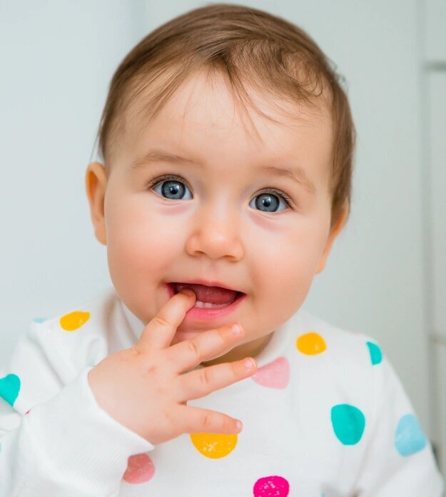Happy baby with finger in mouth during teething stage, showing typical symptoms.