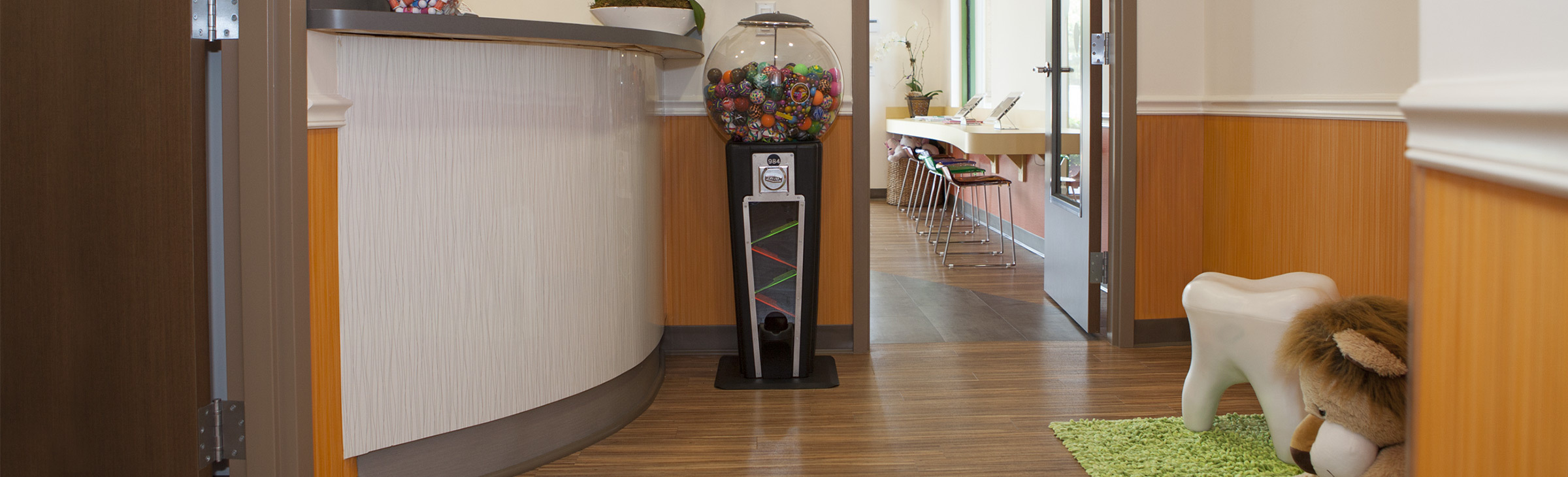 Pediatric dental office waiting room with colorful gumball machine, tooth-shaped seating, and welcoming decor.